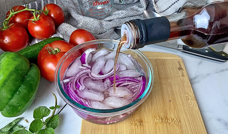 Sliced onions in a bowl of ice water with vinegar being added