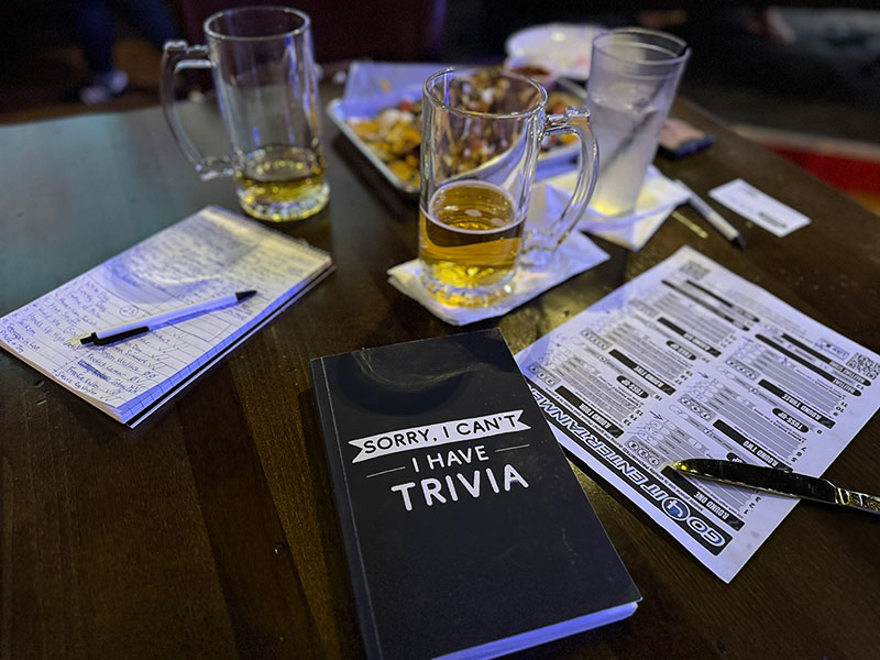 A table with trivia cards, pens, and beer glasses