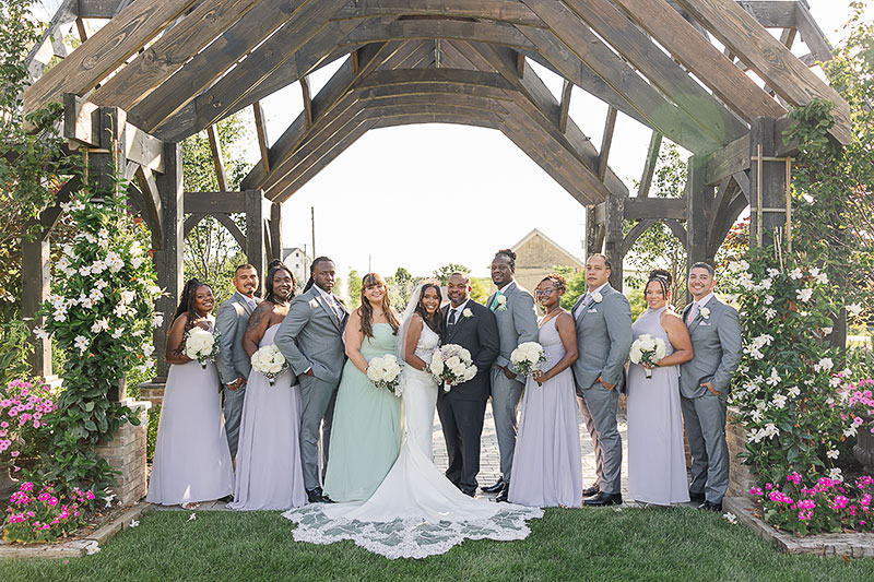 Patrice March-Davidson and Aubrey Davidson posing with their wedding party under a flower-filled archway