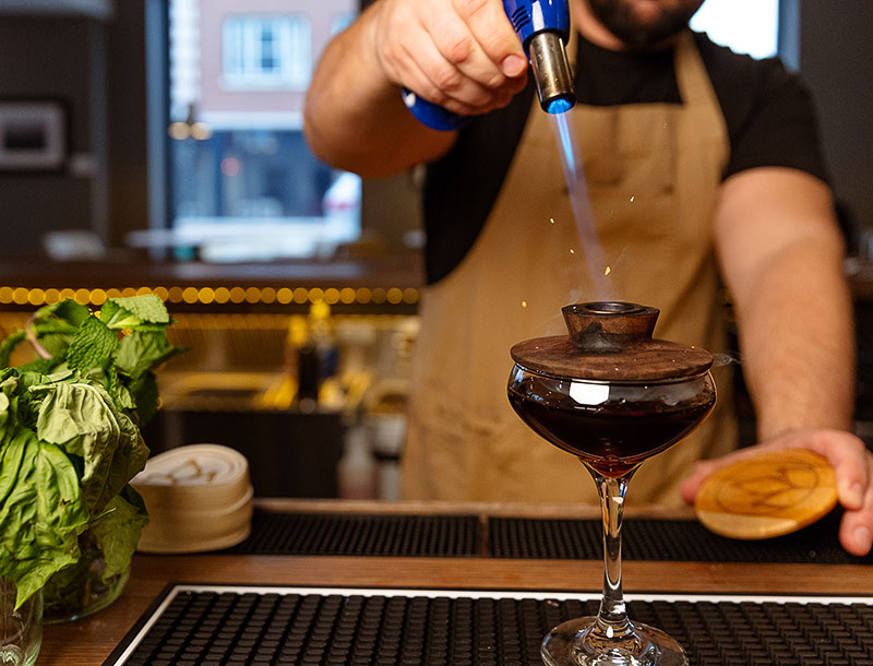 A bartender using a handheld torch on a cocktail at Pollyanna Social