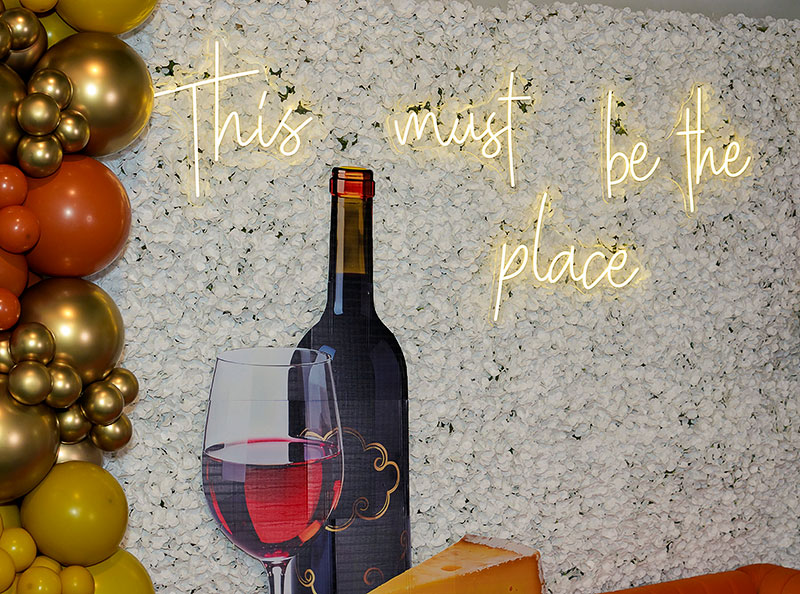 A wall featuring a painted wine bottle and wineglass, with the words "This must be the place" in neon
