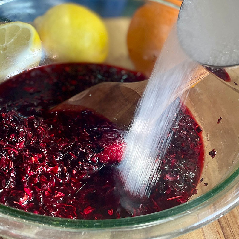 Adding sugar to a bowl of hibiscus flowers to make Hibiscus Citrus Sorbet