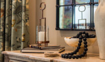 An existing piece of furniture is given a fresh look with a new mirror, a vase with faux blooms, and an alabaster bowl with beads.