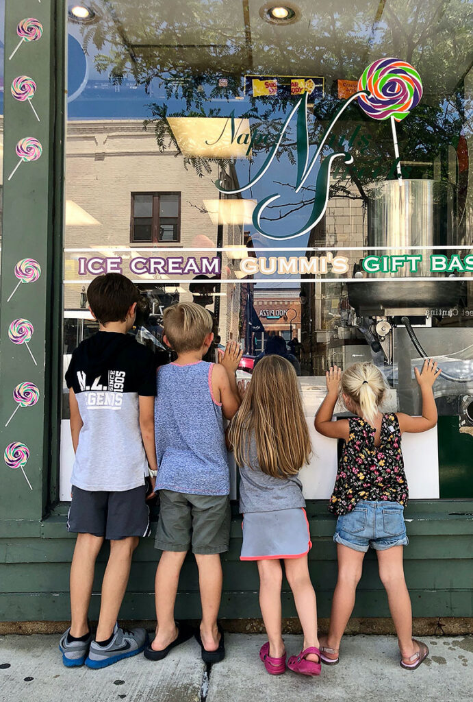 Four young kids looking into the Naper Nuts and Sweets storefront window